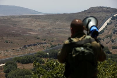An Israeli soldier speaks over a megaphone to people which stand next to the border fence between Israel and Syria from its Syrian side as it is seen from the Israeli-occupied Golan Heights near the Israeli Syrian border July 17, 2018. REUTERS/Ronen Zvulun