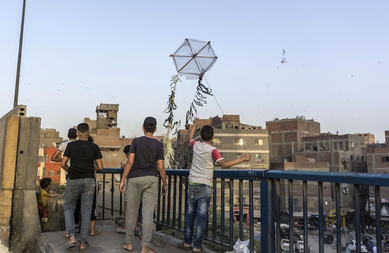 Egyptian youths fly a handmade kite from an overpass on the capital Cairo's Ring Road before "iftar", or breaking the fast at sunset, during the Muslim holy month of Ramadan, on May 22, 2020. / AFP / Khaled DESOUKI
