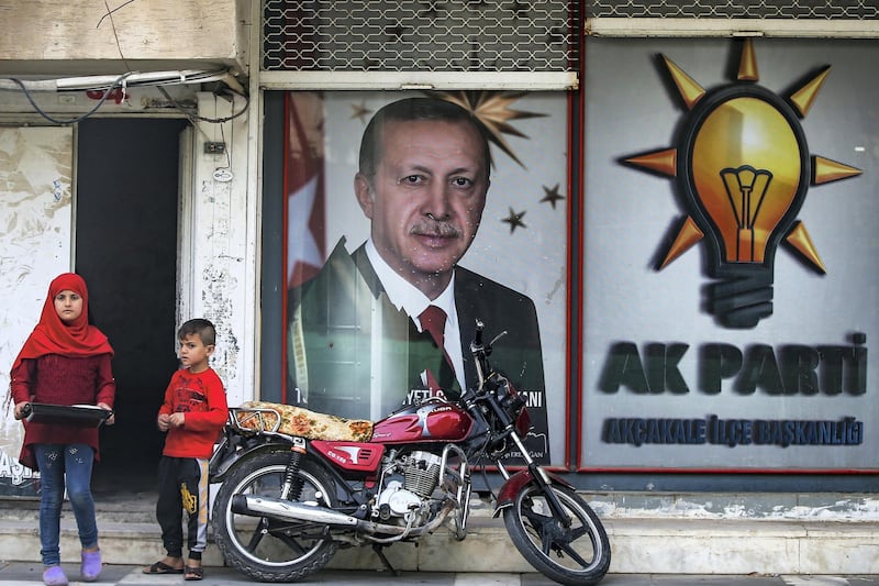 Turkish children stand in front of a billboard with a picture of Turkey's President Recep Tayip Erdogan and a poster of his ruling Justice and Development Party, AKP, in the border town of Akcakale, Sanliurfa province, southeastern Turkey, Friday, Oct. 18, 2019. The cease-fire in northern Syria got off to a rocky start Friday, as Kurdish leaders accused Turkey of violating the accord with continued fighting at a key border town while casting doubt on provisions in the U.S.-brokered deal with Ankara. (AP Photo/Emrah Gurel)
