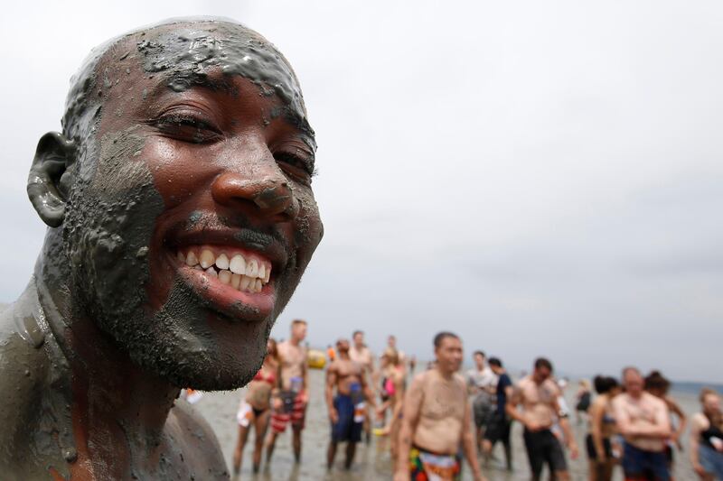 A festival-goer smiles while covered in mud, with a crowd of other revellers behind him. Jeon Heon-Kyun.