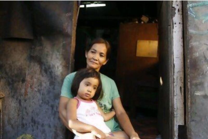 Fe Capco, a beneficiary of government's Conditional Cash Transfer programme holds her daughter Rihanna on her lap at the entrance of their shanty in Pateros in Metro Manila.