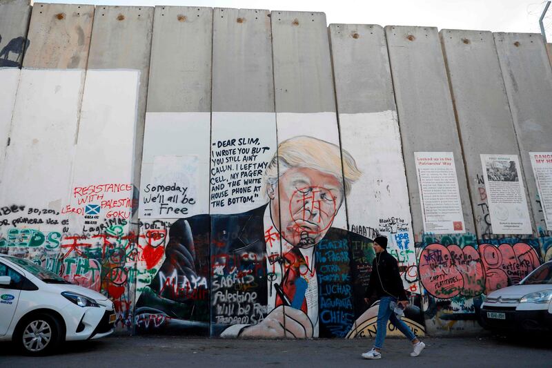 A Palestinian man walks past the vandalised mural painting of US President Donald Trump on Israel's separation barrier in the West Bank city of Bethlehem. AFP