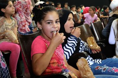 Children eat popcorn as they await the screening of a film at the Cinema Zaatari in the Jordanian Zaatari camp for Syrian refugees, during the opening ceremony of the venue in the camp, about 80 kilometers (50 miles) north of the Jordanian capital Amman, on June 23, 2019. The idea of a 110-seat cinema came when Giannoli, one of the project's founders, worked on a film in the camp with Syrian refugees two years ago. He decided to raise funds for the project, which was named "Lumière Zaatari" in honor of the French pioneer filmmakers, the Lumiere brothers. / AFP / afp / Khalil MAZRAAWI