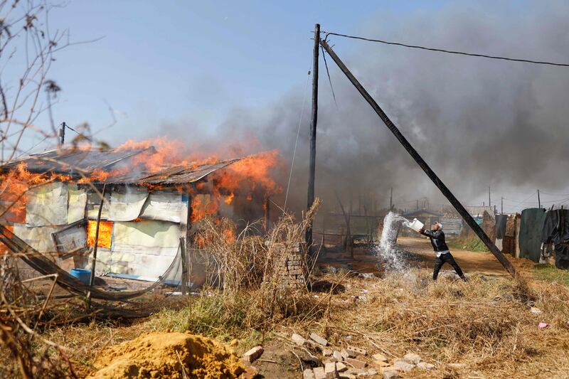 A resident attempts to extinguish a fire after a shack belonging to a man, who was suspected of helping illegal miners in the area, was set on fire by protesters in Kagiso, South Africa. AFP