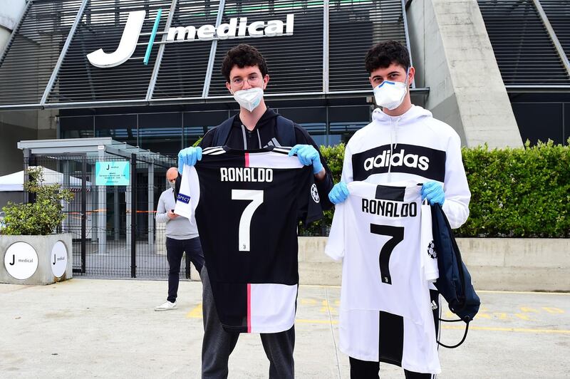 Juventus fans wearing protective face masks and gloves display shirts with Cristiano Ronaldo's name as players and staff arrive for training at Juventus Training Center. Reuters