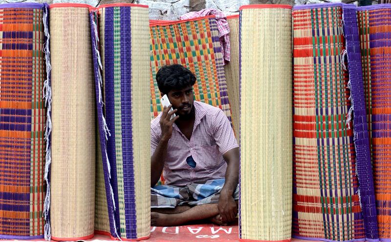 An Indian grass mat vendor speaks on a phone as he waits for customers at a market in Chennai. Arun Sankar / AFP Photo