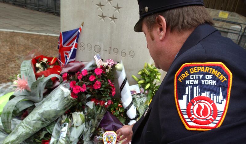 A New York Fire Department officer kneels beside flowers and tributes left outside the embassy on September 11, 2003, the second anniversary of the terrorist attacks on the US. Getty Images