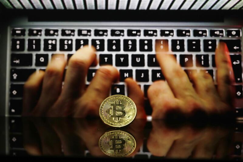 A coin representing Bitcoin cryptocurrency sits reflected on a polished surface and photographed against a backdrop image of hands entering data into a laptop computer in this arranged photograph in London, U.K., on Thursday, Feb. 8, 2018. Cryptocurrencies tracked by Coinmarketcap.com have lost more than $500 billion of market value since early January as governments clamped down, credit-card issuers halted purchases and investors grew increasingly concerned that last year’s meteoric rise in digital assets was unjustified. Photographer: Luke MacGregor/Bloomberg /Bloomberg