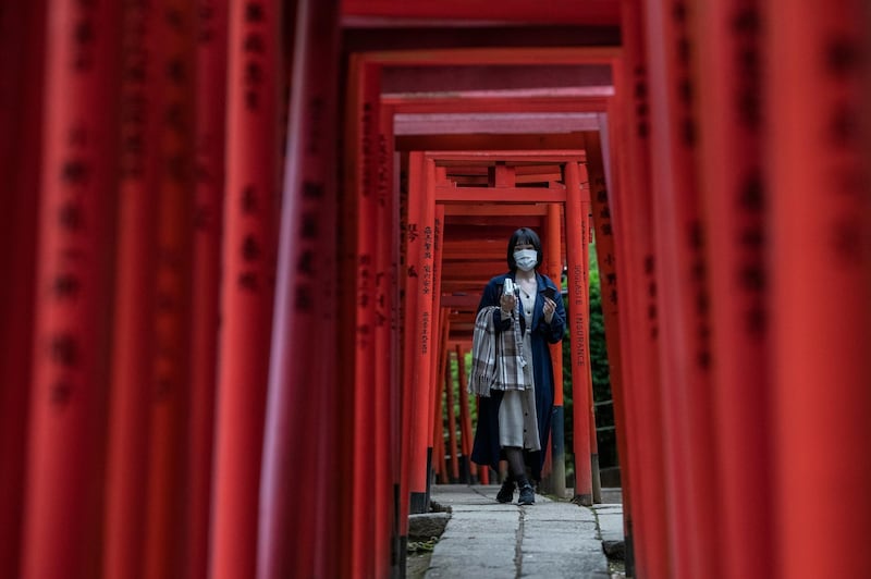 A woman wearing a face mask walks under torii gates as she visits a Shinto shrine in Tokyo, Japan. Getty Images