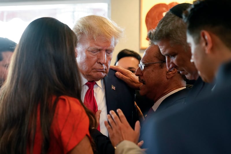 Mr Trump prays with pastor Mario Bramnick and others at Versailles restaurant after his court hearing. AP