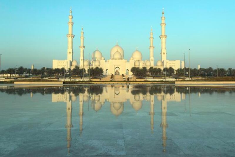 A man walks past the central water feature at Wahat Al Karama, a shallow pool designed to capture the reflections of The Memorial and the Sheikh Zayed Grand Mosque. Christopher Pike / The National