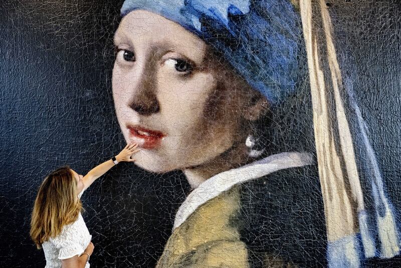 A woman touches the surface of an enlarged version of the famous painting 'Girl with a Pearl Earring' by Johannes Vermeer at the 'Mauritshuis' museum in The Hague, The Netherlands, 08 June 2023.  The Vermeer painting has been enlarged a 100-times as a 3D print to become a four-meters high plastic colossus which is exhibited in the foyer of the museum.  The giant 3D print clearly shows how the canvas has developed over the years and which painting techniques have been used.   EPA / ROBIN UTRECHT