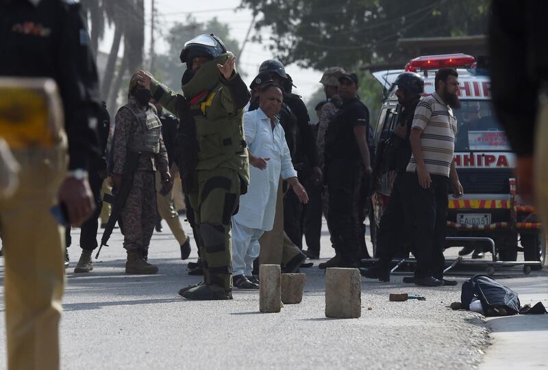 A bomb disposal squad member warns onlookers before checking a bag belonging to an attacker outside the Chinese consulate in Karachi. AFP