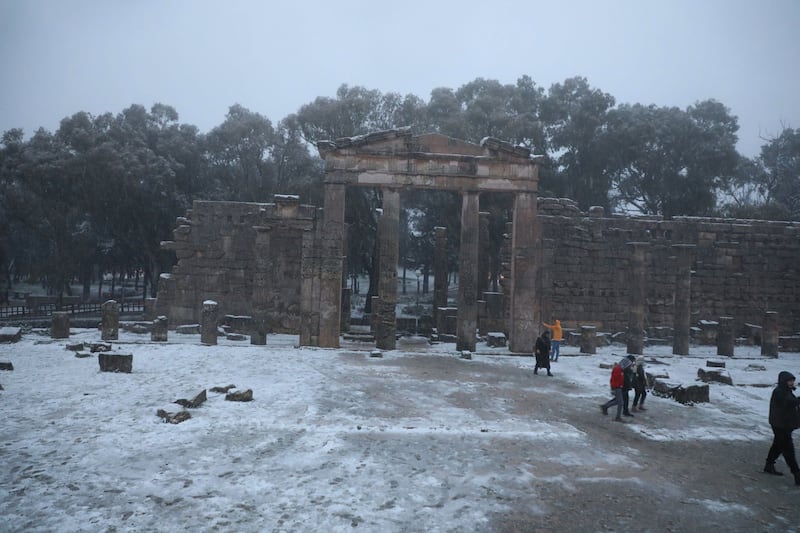 People wander in the ruins of Shahhat during the snowfall.