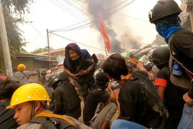 Protesters use slingshots while taking cover behind a barricade as smoke rises from burning debris during ongoing protests against the military coup, in Monywa. Reuters