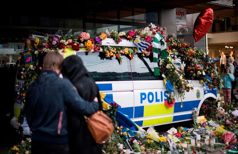 (FILES) In this file photo taken on April 10, 2017 a couple hugs in front of a flower covered police car at the site where a truck drove into a department store in Stockholm, Sweden.
 After pledging allegiance to the Islamic State group, he launched a delivery truck into a crowded Stockholm pedestrian street in April 2017, killing five people. The convicted will face his sentence on Thursday, June 7, 2018. / AFP / Jonathan NACKSTRAND
