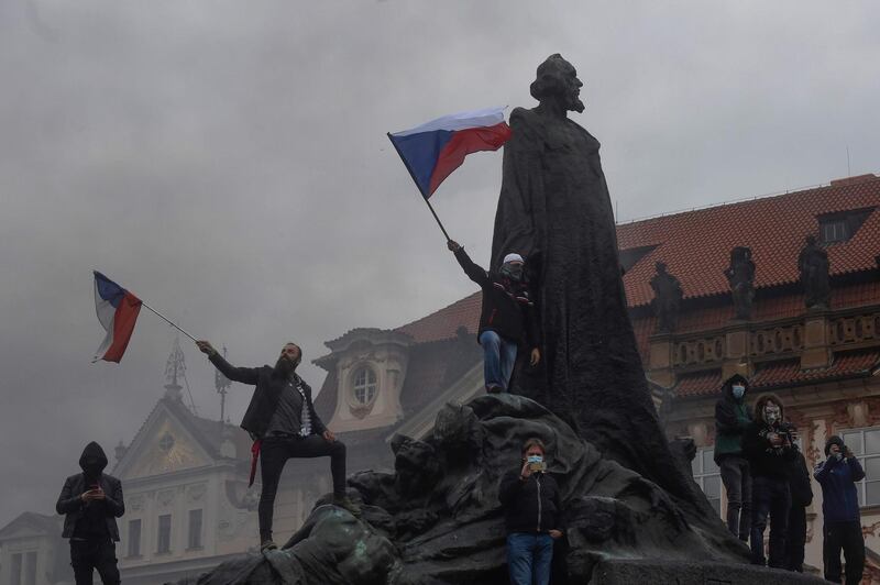 Protestors wave Czech flags as they stand on the statue of Jan Hus at the Old Town Square as hundreds of demonstrators, mostly football supporters, protest against the Czech government's new measures to slow the spread of the coronavirus in Prague.  AFP