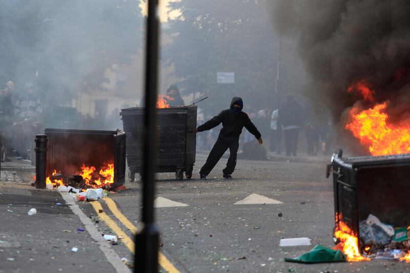 A masked youth pulls a burning garbage bin set on fire by rioters in Hackney, east London, Monday Aug. 8, 2011. Youths set fire to shops and vehicles in a host of areas of London _ which will host next summer's Olympic Games _ and clashed with police in the nation's central city of Birmingham, as authorities struggled to halt groups of rampaging young people. (AP Photo/Lefteris Pitarakis) *** Local Caption ***  Britain Riots.JPEG-04ae0.jpg