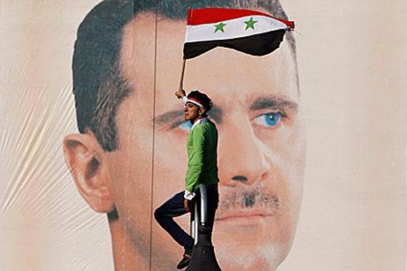 A pro-Syrian regime protester waves a Syrian flag as he stands in front of portrait of Bashar Al Assad in Damascus earlier this month.