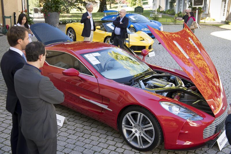 People look at a Aston Martin One-77 Coupe (2011) in front of a Ferrari LaFerrari (2015), yellow, and a Bugatti Veyron EB 16.4 Coupe (2010). The Aston went for 1.55 million francs. EPA