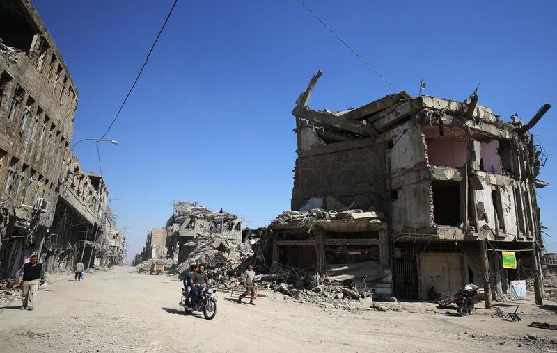 Iraqis pass destroyed buildings in the old city of Mosul on March 14, 2018, eight months after the Iraqi government forces retook the city from the control of the Islamic State (IS) group. / AFP PHOTO / AHMAD AL-RUBAYE