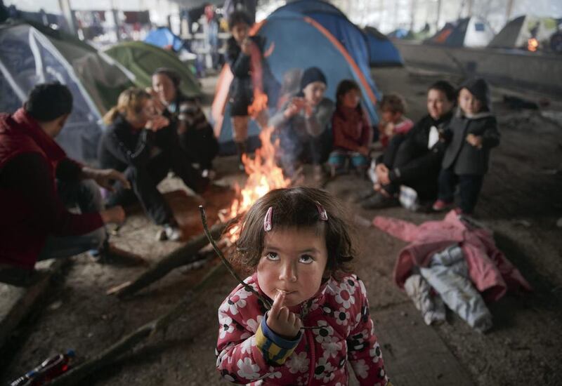 A child eats as other migrants sit around a fire in a railway repairs hangar at Idomeni on the Greece-Macedonia border on March 18, 2016. Vadim Ghirda / AP Photo