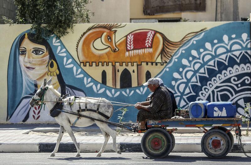 Palestinians ride a donkey cart past a mural along a street in Rafah, in the southern Gaza Strip. AFP