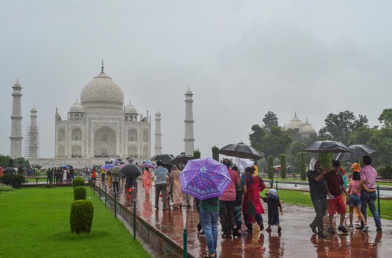 Tourists hold umbrellas as they visit the Taj Mahal under heavy rain in Agra on August 17, 2019. (Photo by STR / AFP)