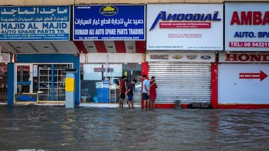 People stand in front of shops on a flooded street in Sharjah on April 20. Small and medium-sized businesses felt the brunt of storms in the UAE. AFP