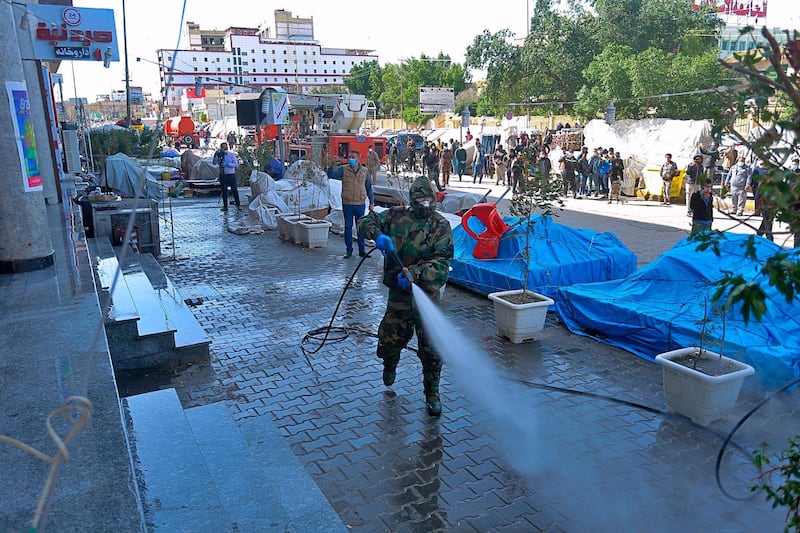 Iraqi health officials and Civil Defense staff wearing protective suits spray disinfectant as a precaution against the coronavirus in the commercial markets in Najaf, Iraq,  AP