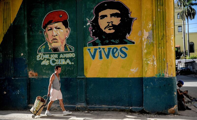 A Cuban passes by a graffiti depicting Venezuelan president Hugo Chavez (L) and Che Guevara in Havana, on July 12, 2017. / AFP PHOTO / YAMIL LAGE