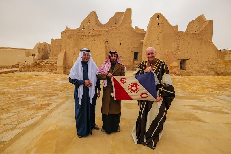Mr Evans holds up the Explorers Club flag with officials from the Saudi Ministry of Culture ahead of the second leg of the Heart of Arabia expedition