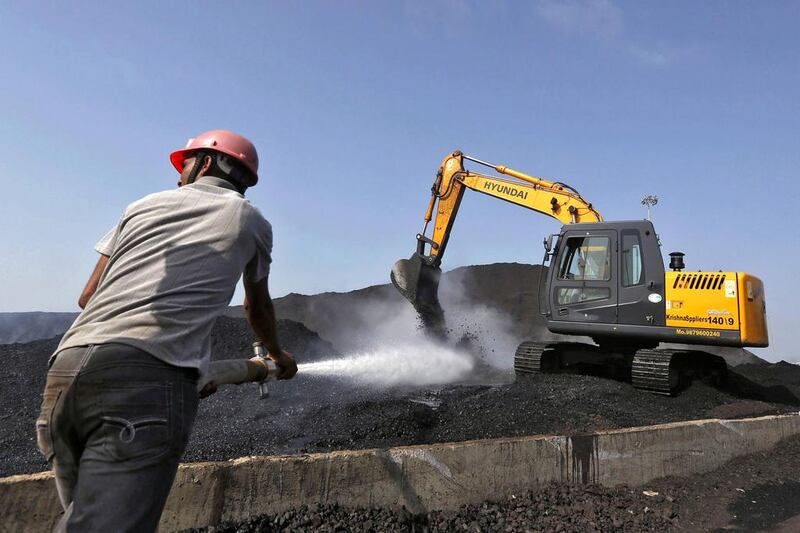 A worker sprays water over piles of coal as a bulldozer shifts coal at Mundra Port Coal Terminal. Amit Dave / Reuters