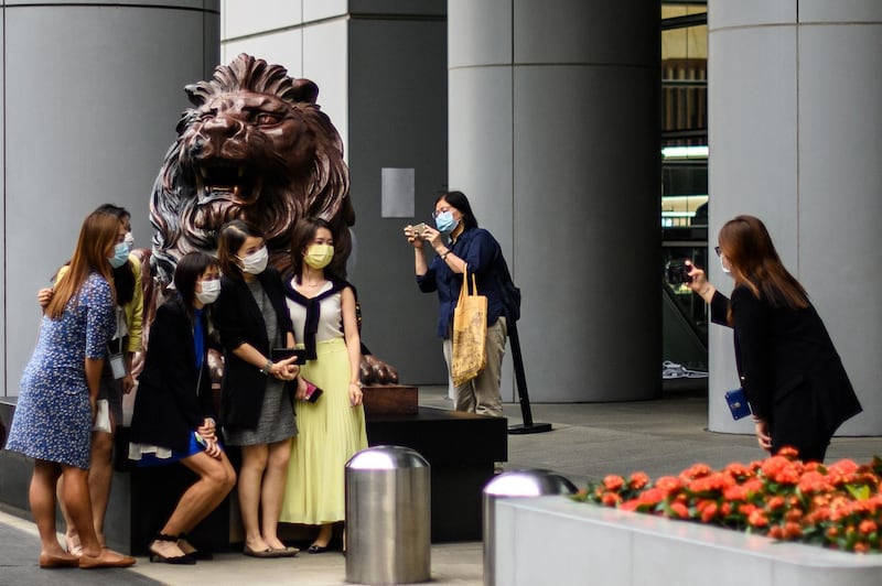 People pose for a photo next to a lion statue outside HSBC bank headquarters building in Hong Kong. AFP