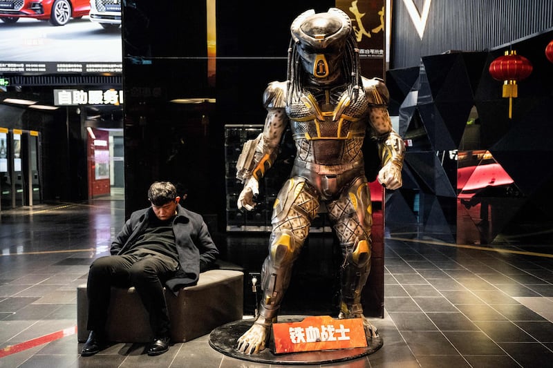 A man naps by a life-size statue of the Predator film character at a mall in Beijing. AFP
