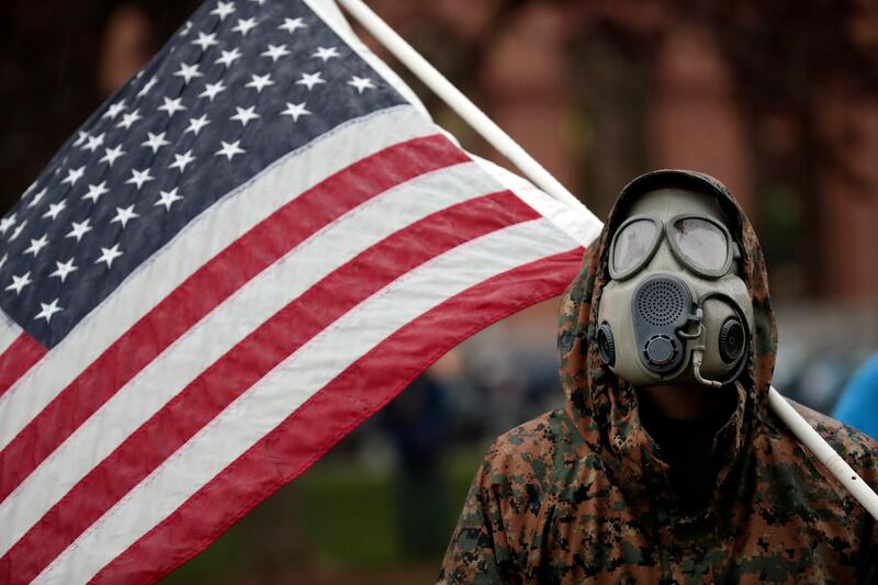 A protester wears a gas mask and carries an American flag during a rally in response to Michigan’s coronavirus stay-at-home order at the State Capitol in Lansing, Michigan. AP