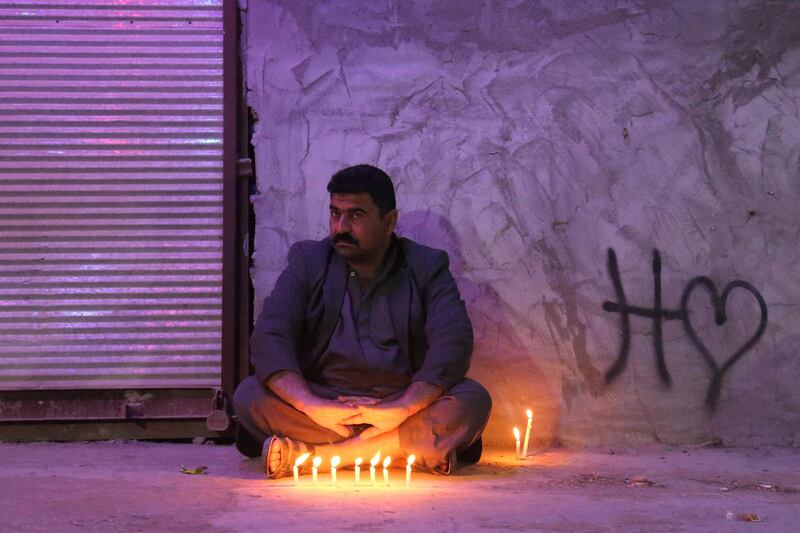 A Shiite Muslim pilgrim sits by lit candles outside the Shrine of Imam Mohammed al-Mahdi during the Shaabaniya ceremony, marking the middle of the Islamic month of Shaban and two weeks before the start of the holy fasting month of Ramadan, and on which Twelver Shiites commemorate the birth of Imam Mahdi (the sect's final Imam), in Iraq's central holy shrine city of Karbala on March 28, 2021.  / AFP / Mohammed SAWAF
