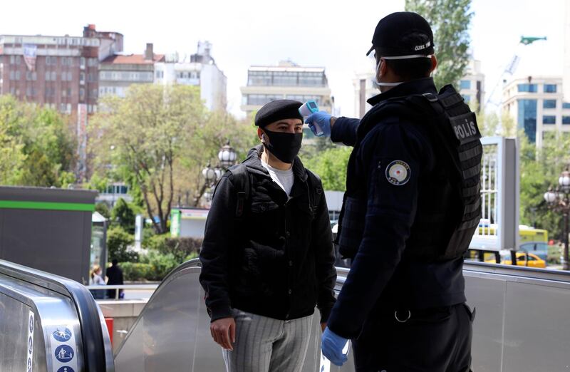 A police officer, wearing a face mask for protection against the coronavirus, checks a person's body temperature, in Ankara, Turkey. AP Photo