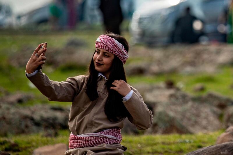 A woman dressed in traditional Syrian Kurdish clothing poses for a selfie in a meadow as people celebrate the spring holiday of Noruz in the town of Qahtaniyah. AFP