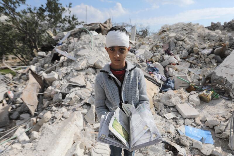 A Syrian boy, who lost his family in the deadly earthquake, stands amid the rubble of his family home in Jindayris. AFP
