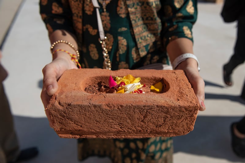 A woman carries a brick to be placed at the site of the BAPS Hindu Mandir temple after a prayer ritual.