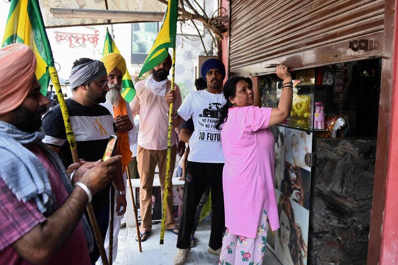 Farmers urge a shopkeeper to open her shop in the north-west Indian city of Amritsar, as they take part in a protest against the weekend coronavirus lockdown imposed by the Punjab state government.