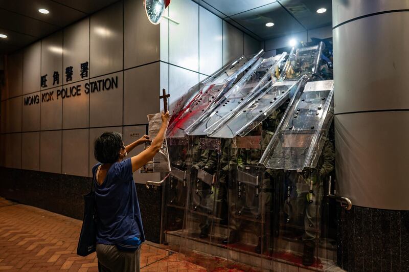 A woman holds a cross in front of the Mongkok Police Station as riot police holding shields stand guard during a standoff with protesters after an anti-government rally in Hong Kong.  Getty Images