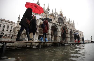 People walk on catwalk set up in front of St. Mark's Basilica on the occasion of a high tide, in a flooded Venice, Italy, Tuesday, Nov. 12, 2019. The high tide reached a peak of 127cm (4.1ft) at 10:35am while an even higher level of 140cm(4.6ft) was predicted for later Tuesday evening. (AP Photo/Luca Bruno)