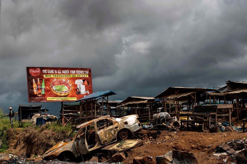 The wreckage of burnt out car is pictured, allegedly destroyed by separatists fighter in a recent attack, as a Cameroonian soldier (L) patrols the edge of the abandoned market in the majority anglophone South West province in Buea, on October 3, 2018. / AFP / MARCO LONGARI
