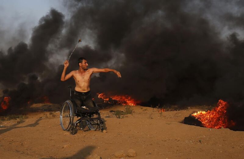 A Palestinian protester on a wheelchair throws a stone toward Israeli forces during clashes along the Israeli border fence, east of Gaza City. AFP