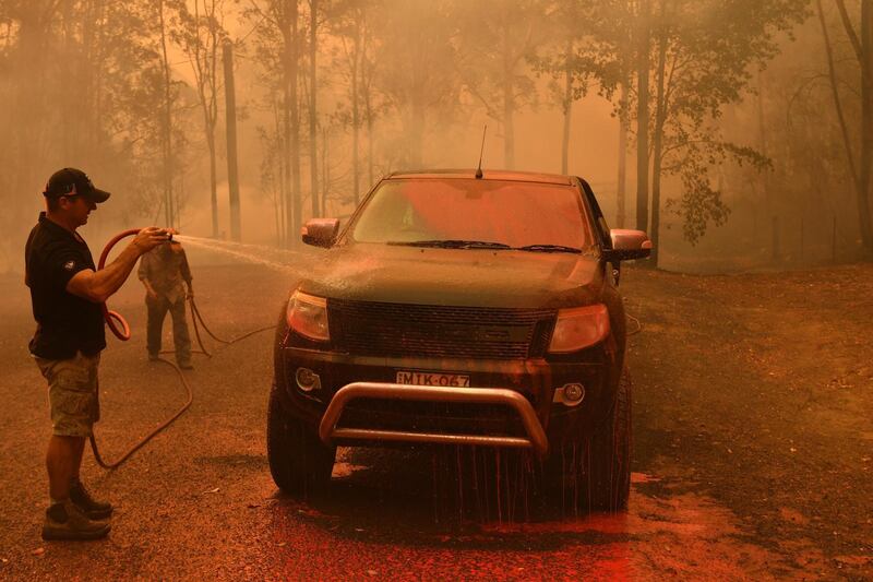A local man hoses down fire retardant from a vehicle during a bushfire in Werombi, 50km south west of Sydney, Australia.  EPA