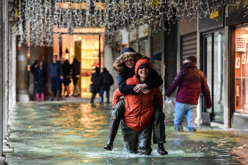 TOPSHOT - A person carries another across a flooded arcade on November 24, 2019 in Venice during a high tide "Acqua Alta" meteorological phenomenon with a high of 140 cm expected. Flood-hit Venice was bracing for another, though smaller, high tide on November 24, after Italy declared on November 15 a state of emergency for the UNESCO city where perilous deluges have caused millions of euros worth of damage. / AFP / Miguel MEDINA
