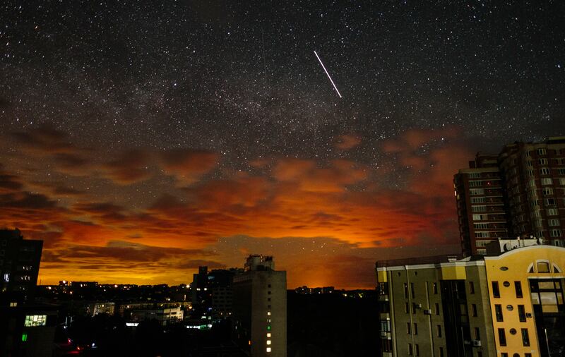 The orange glow of continuing battle is projected on to the clouds as a satellite crosses the starry sky above Kharkiv, Ukraine. EPA