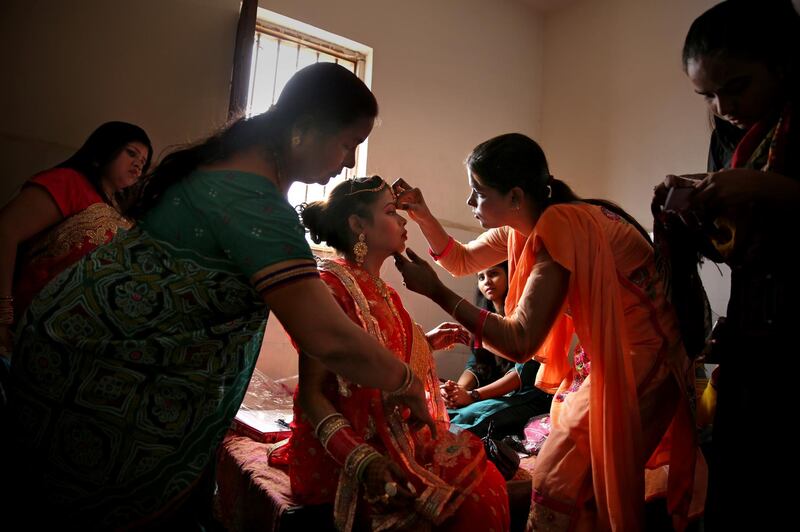 Family members apply makeup on an Indian bride before a mass marriage ceremony for eight couples in New Delhi, India, Friday. Mass weddings in India are organized by social organizations primarily to help economically backward families who cannot afford the high ceremony costs as well as the customary dowry and expensive gifts that are still prevalent in many communities. AP Photo